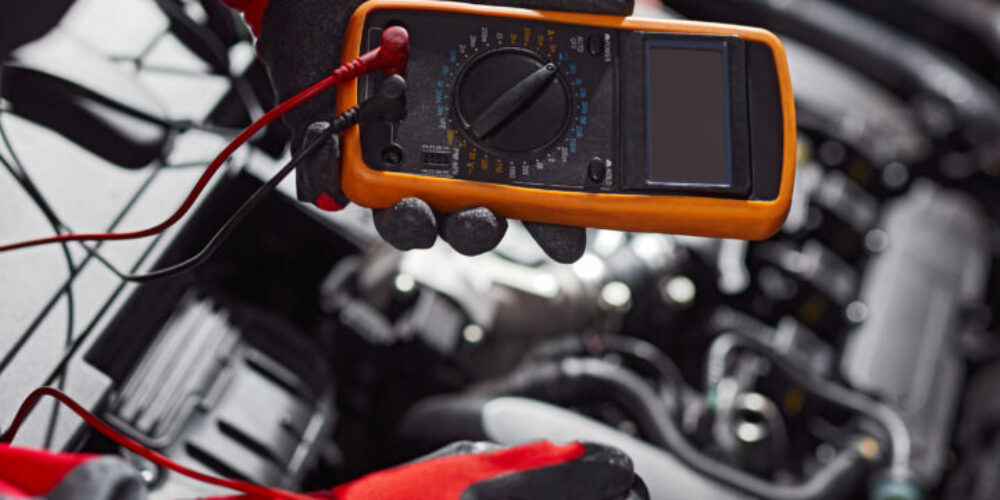 High angle side view of crop unrecognizable male technician using multimeter while doing voltage test of automobile battery in professional service center